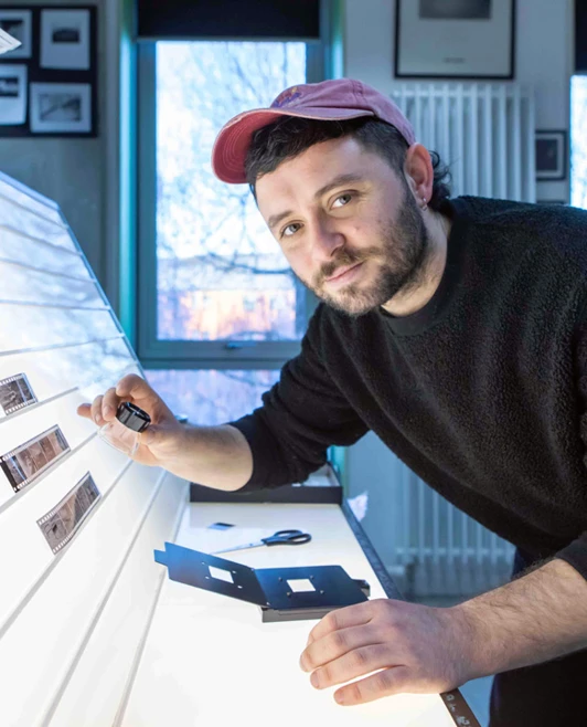 Student examining black and white film negatives on a lightbox in a photography studio. Student examining black and white film negatives on a lightbox in a photography studio.